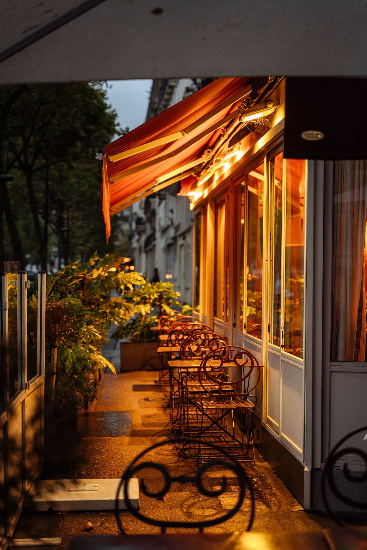 Terrasse d'un café parisien au crépuscule, chaises en fer forgé sous l'auvent